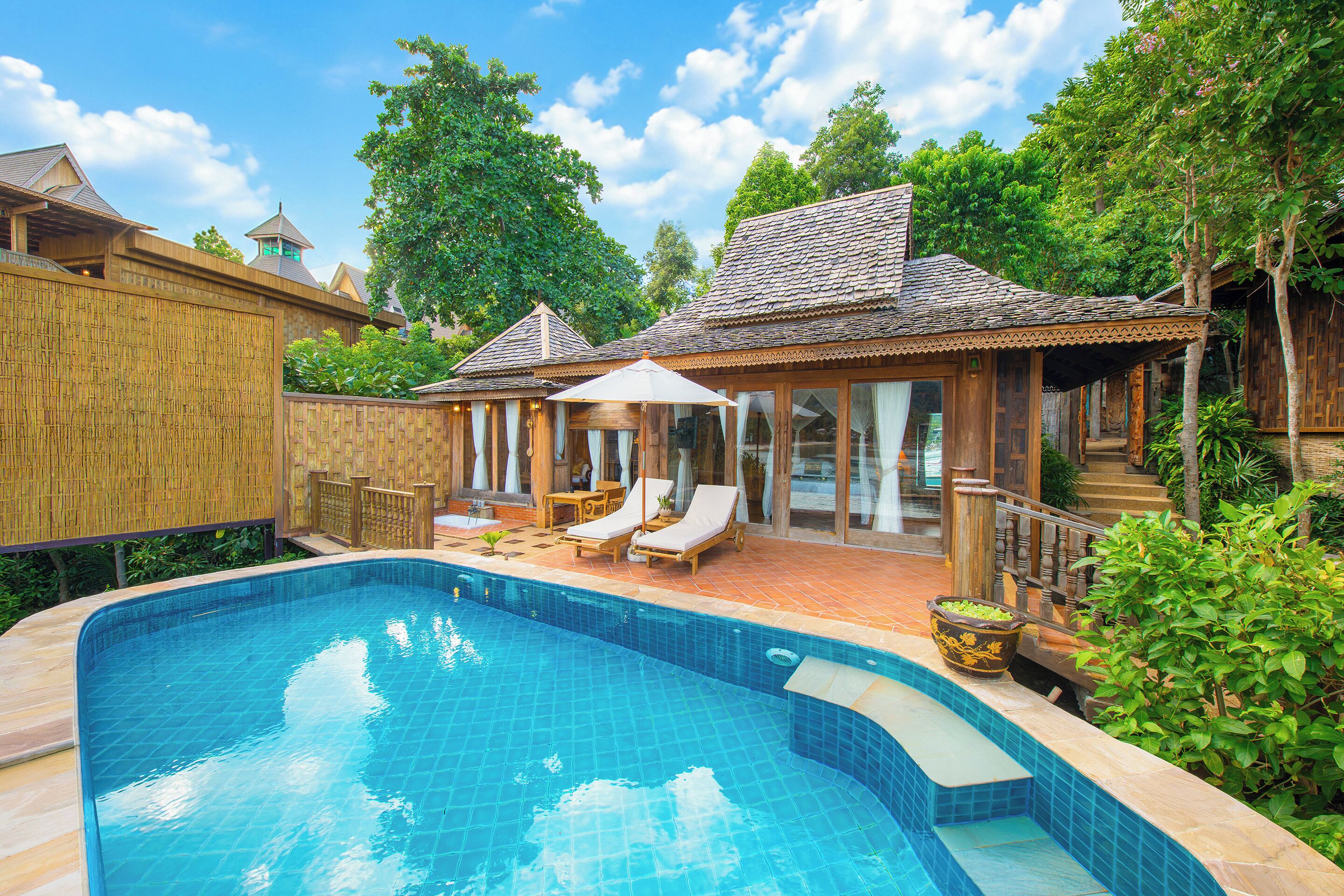 A swimming pool with a wooden deck, lounge chairs, and a covered seating area.