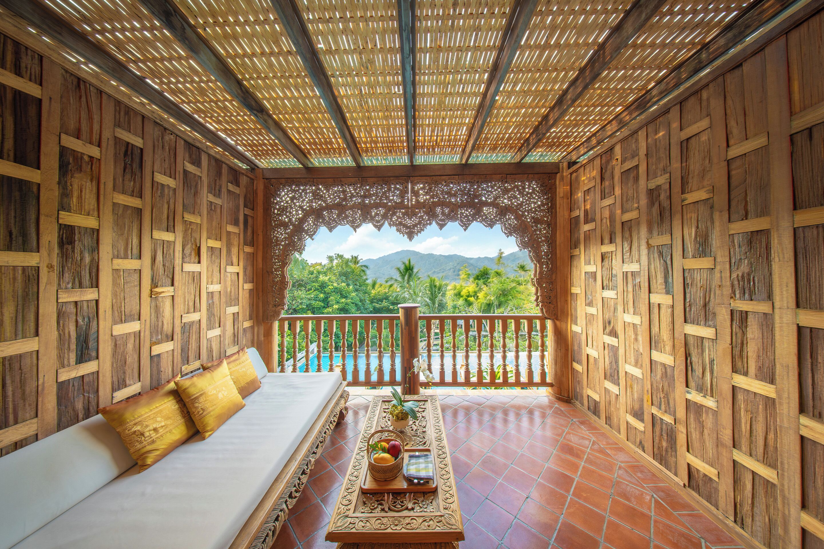 A wooden room with a balcony, a white sofa, and a table with fruit and a bottle.