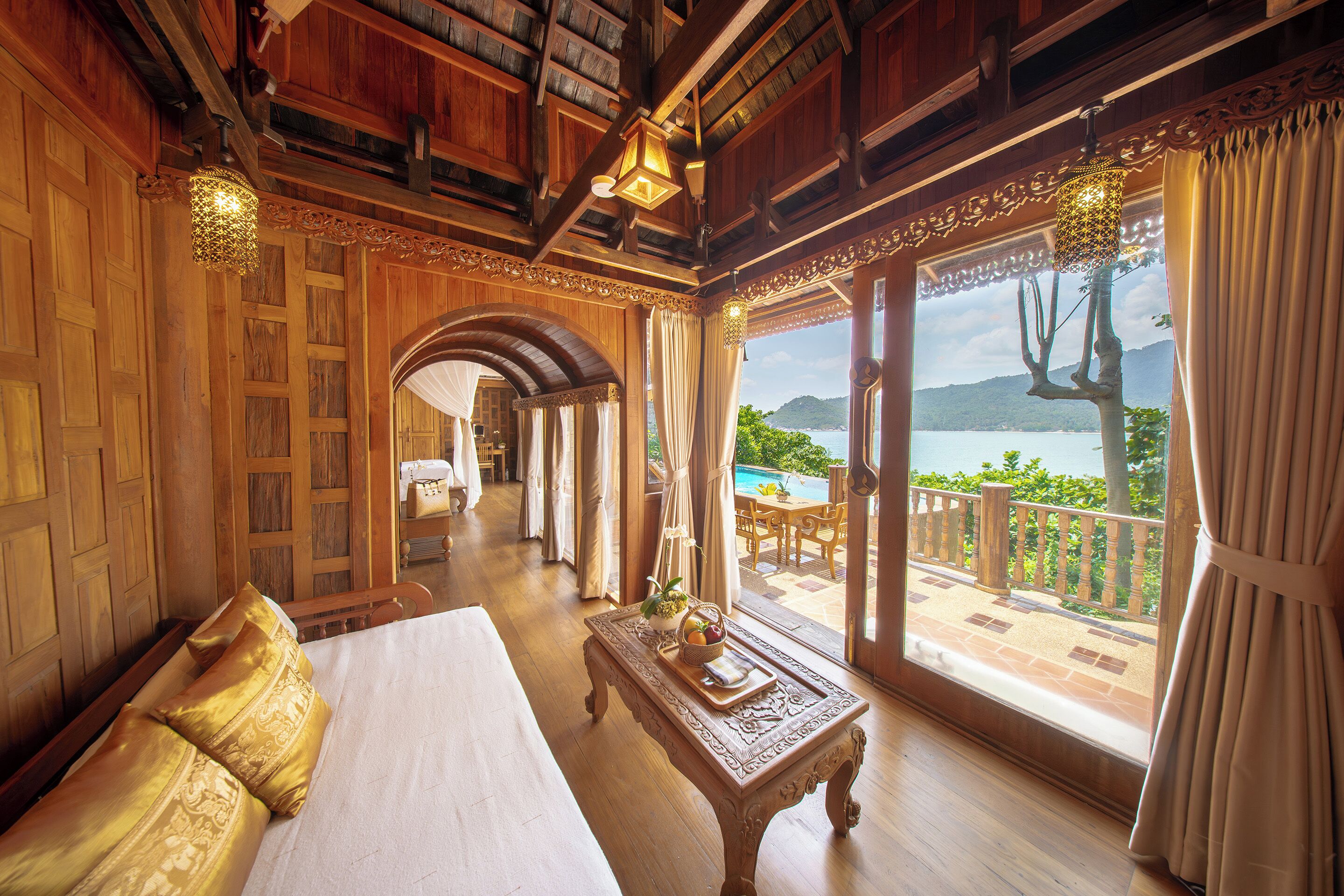 A hotel room with a large bed, a wooden coffee table, and a view of a pool and mountains.