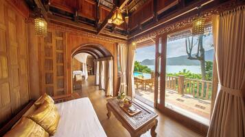 A hotel room with a large bed, a wooden coffee table, and a view of a pool and mountains.