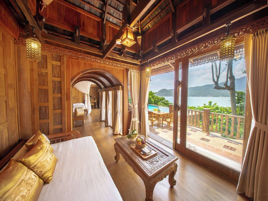 A hotel room with a large bed, a wooden coffee table, and a view of a pool and mountains.