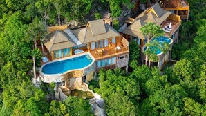 An aerial view of a resort with multiple buildings, a large swimming pool, and lush greenery surrounding the property.