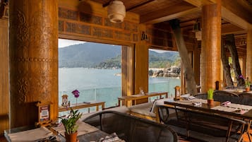 Un espace extérieur aménagé pour les repas, avec des meubles en bois, une vue sur la mer et des colonnes décoratives.
