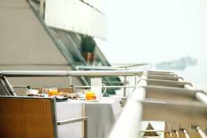 A table set with breakfast items, including a glass of orange juice, a cup, and a plate with food, on a balcony with a railing and a view of the sea. - Daios Luxury Living (Thessaloniki)