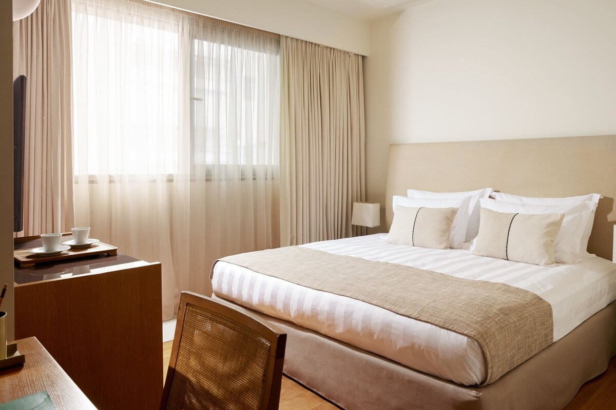 A hotel room with a bed, a desk, a chair, and a TV.