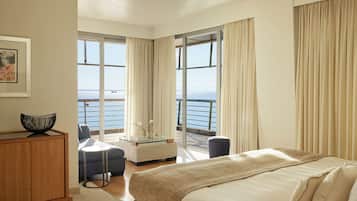 A hotel room with a bed, a seating area with a table, a view of the sea, and a balcony with curtains.