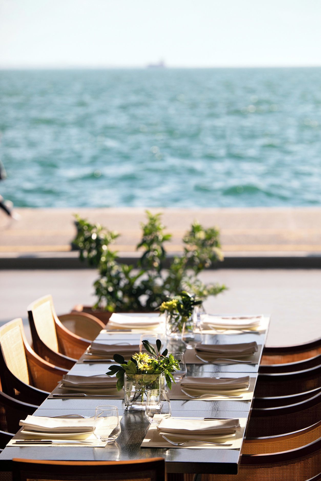 A dining table set with plates, glasses, and cutlery, overlooking a body of water.