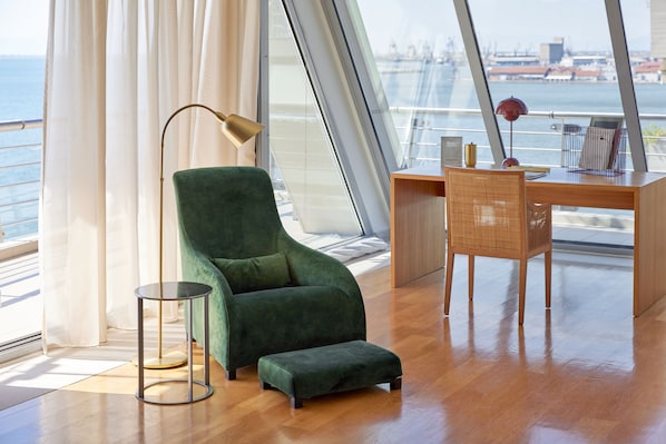 Una habitación moderna con un sillón verde, un escritorio de madera y vistas a un puente y al agua.
