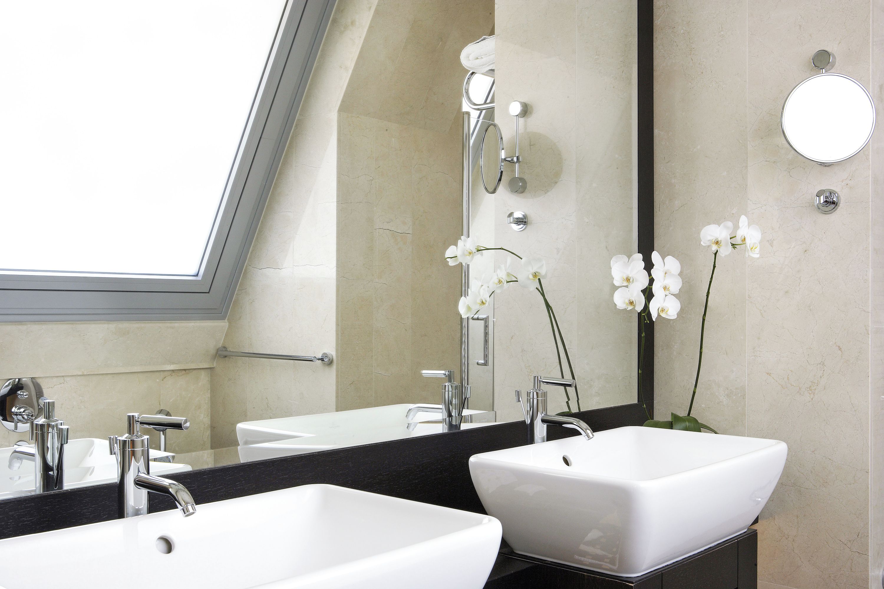 A modern bathroom with two white sinks, a large mirror, and a skylight.