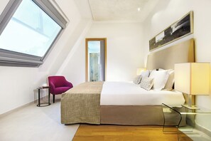 A hotel room with a bed, a chair, a bedside table with a lamp, a window, and a painting on the wall.