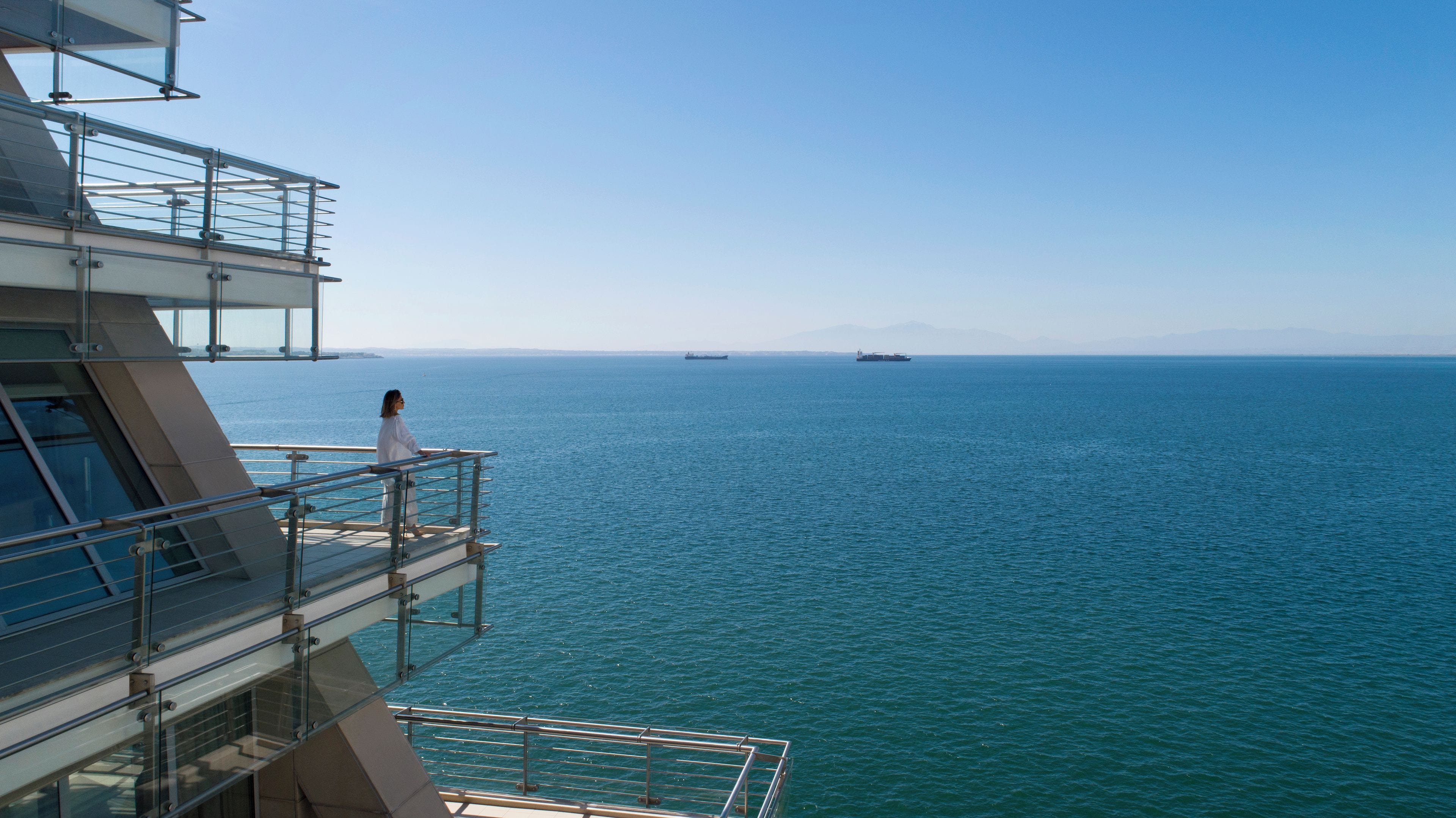 Un balcón con vista al mar y barcos a lo lejos.