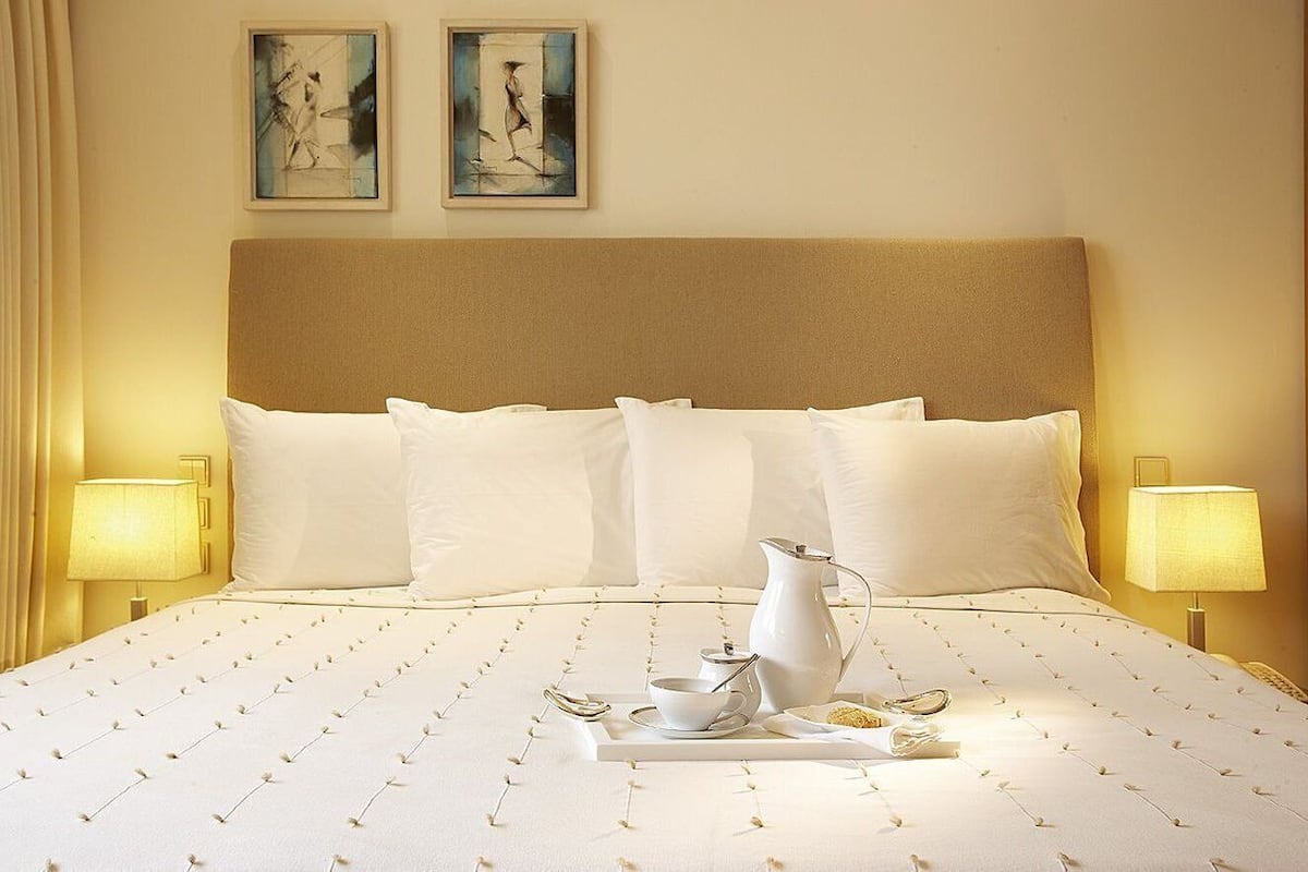 Een hotelkamer met een groot bed, twee bedlampen, een dienblad met ontbijtartikelen en twee ingelijste kunstwerken aan de muur.
