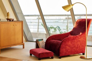 Una habitación moderna con un sillón tapizado en terciopelo rojo, un reposapiés a juego, un armario de madera y una lámpara de pie.