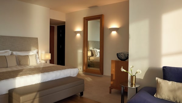 A hotel room with a bed, bedside lamps, a mirror, a small table with a vase, and a blue armchair.