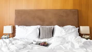 Een netjes opgemaakt bed met witte lakens, een bruin hoofdbord en een dienblad met een kopje en druiven.