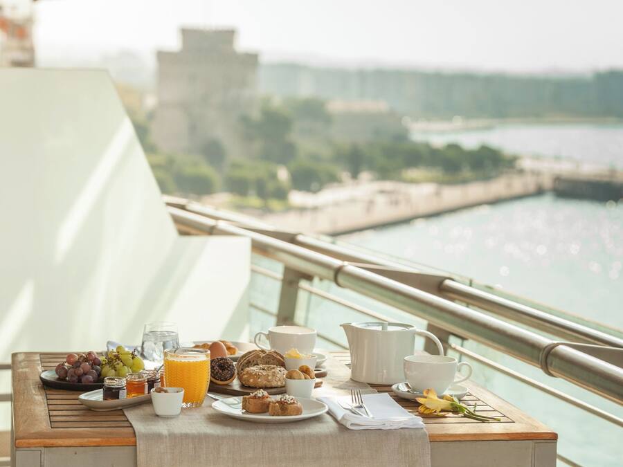 A breakfast table with various food items and a view of a river and buildings in the background.