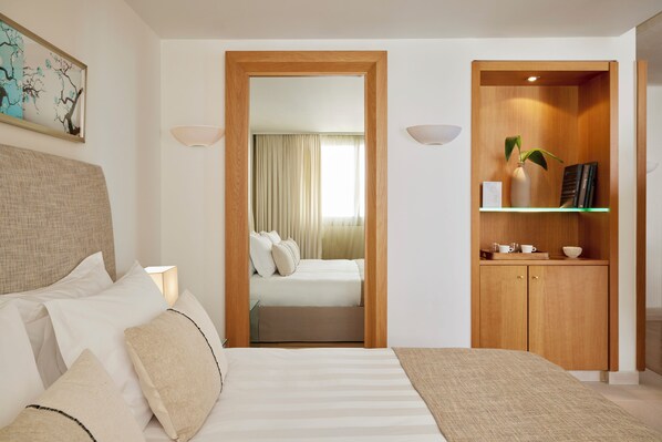 A hotel room with a bed, a bedside lamp, a wooden cabinet with a plant, and a framed picture on the wall.