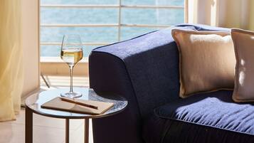 Ein Zimmer mit einer Couch, einem kleinen runden Tisch, einem Glas Weißwein und einem Fenster mit Blick.