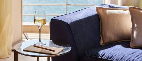 Una habitación con sofá, una mesita redonda, una copa de vino blanco y una ventana con vistas.