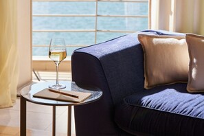 Una habitación con sofá, una mesita redonda, una copa de vino blanco y una ventana con vistas.
