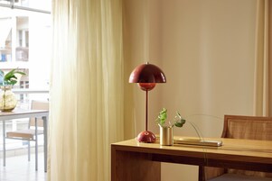 Una mesa de madera con una lámpara de pie roja, una planta pequeña y un libro.