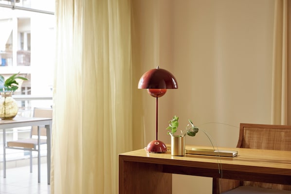 Une table en bois, une lampe de sol rouge, une petite plante et un livre.