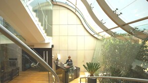 Een modern interieur met een gebogen glazen plafond, een receptiebalie en een trap.