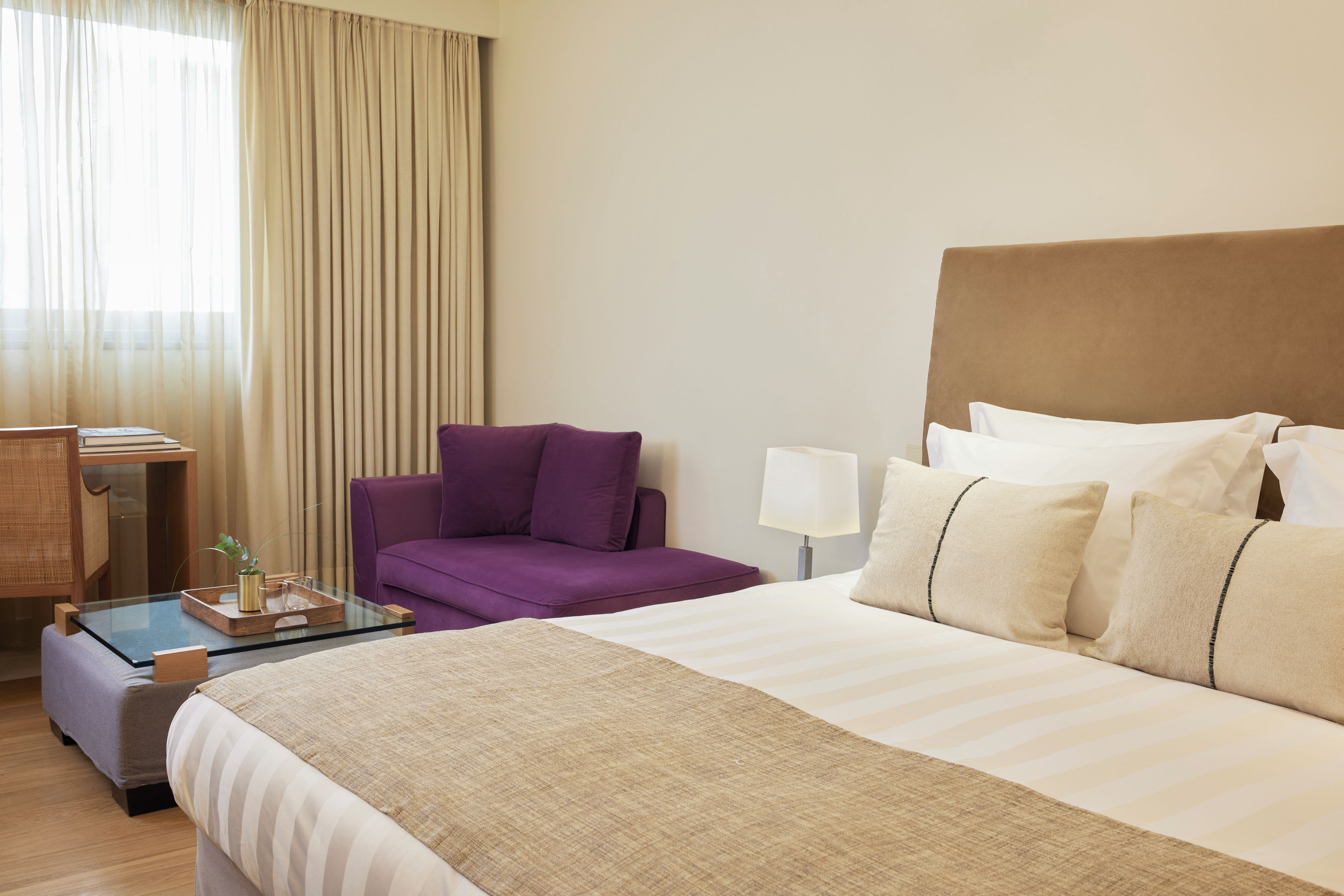 A hotel room with a bed, a sofa, a desk with a lamp, and a window with curtains.