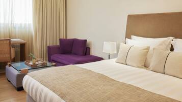 A hotel room with a bed, a sofa, a desk with a lamp, and a window with curtains.