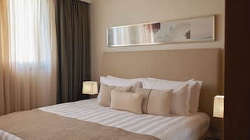 A hotel room with a large bed, a headboard, two bedside lamps, and a painting on the wall.
