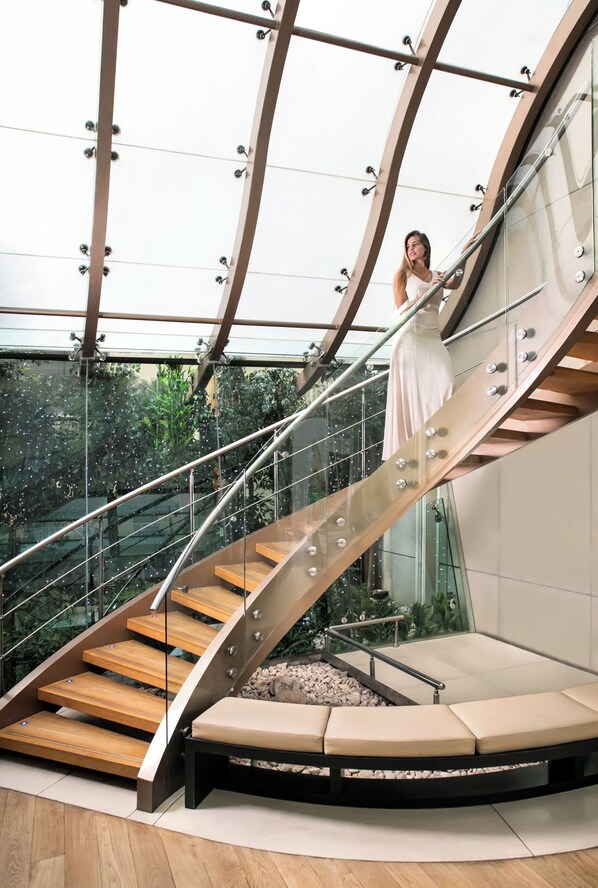 Una escalera interior moderna con barandillas de vidrio y peldaños de madera.