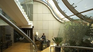 Een modern interieur met een gebogen glazen dak, een receptiebalie en een trap.