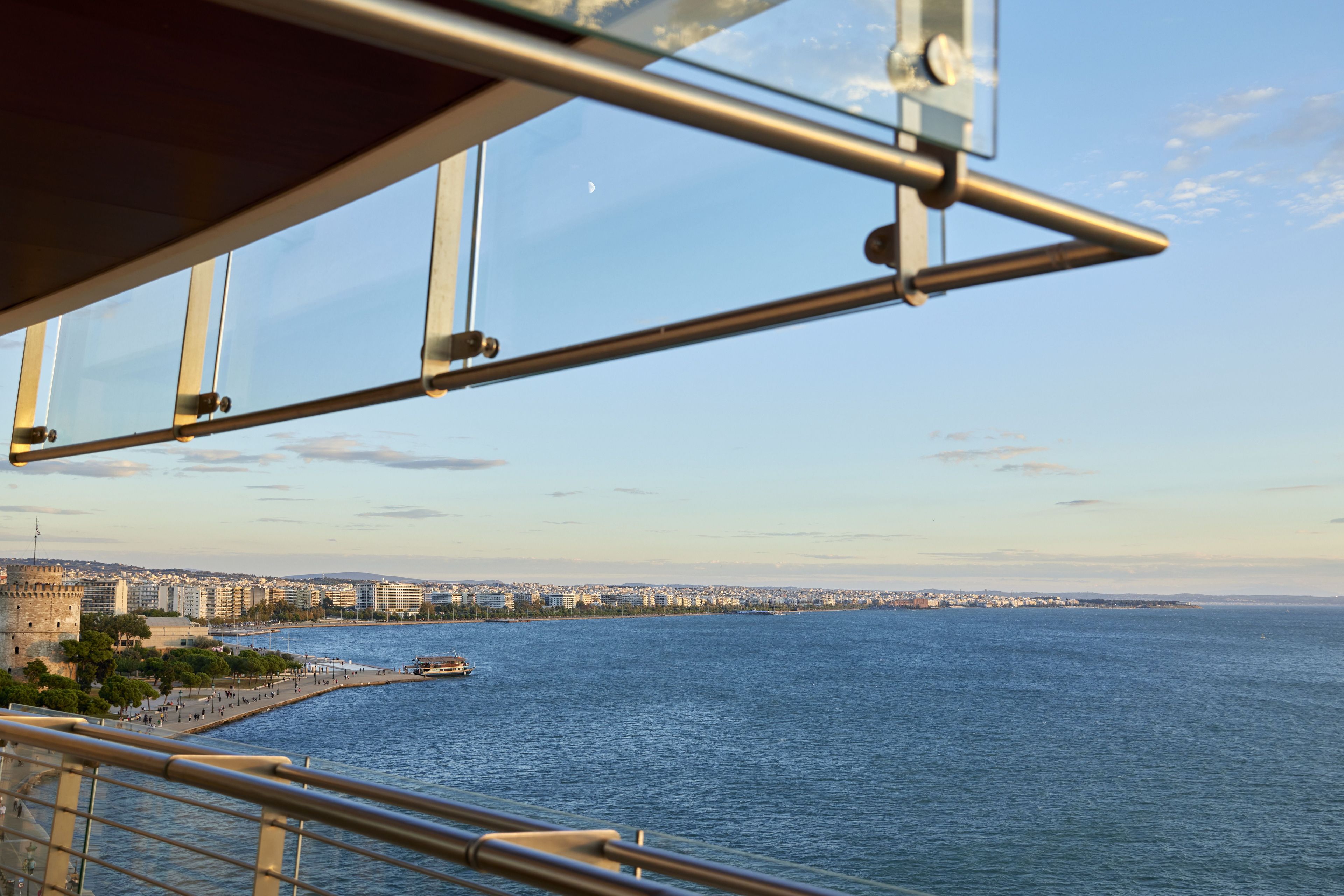 Un paisaje costero urbano con vista despejada al mar, una estructura imponente que recuerda a un castillo y un edificio moderno con fachada de vidrio.