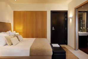 Une chambre d’hôtel moderne avec un grand lit, une armoire en bois, une porte noire et une salle de bain équipée d’un lavabo et d’un miroir.