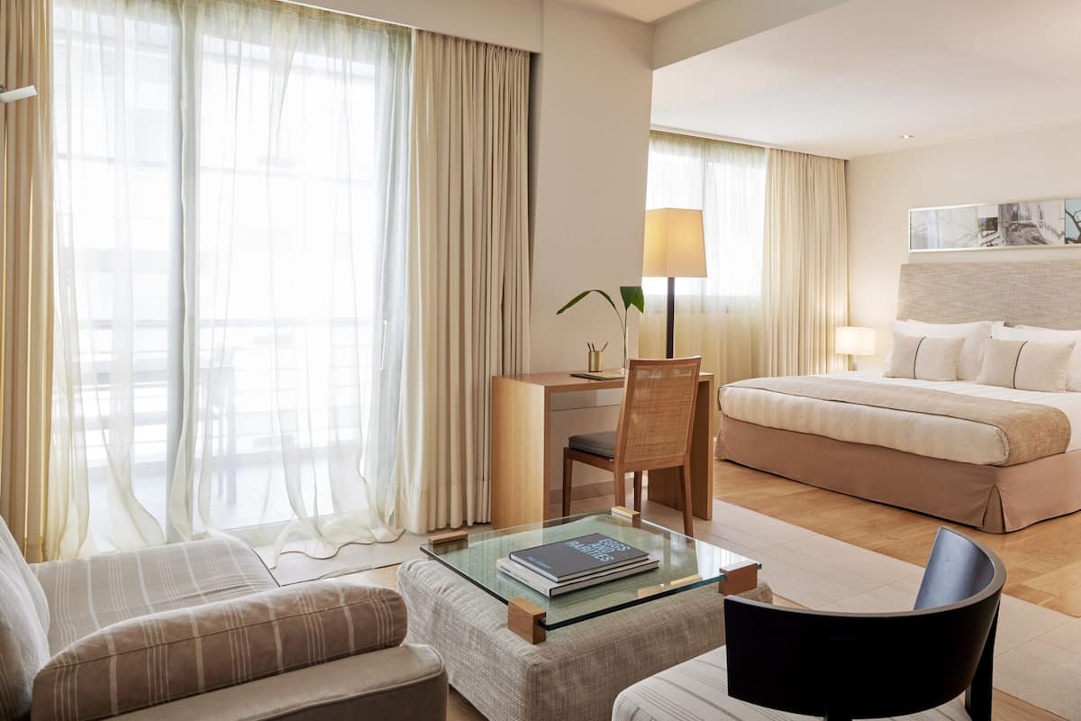 Een hotelkamer met een bed, een bureau, een stoel, een bank en een glazen bijzettafeltje.