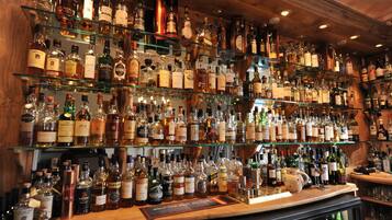 Stocked bar area with a selection of liquor bottles on glass shelves and a wooden counter.