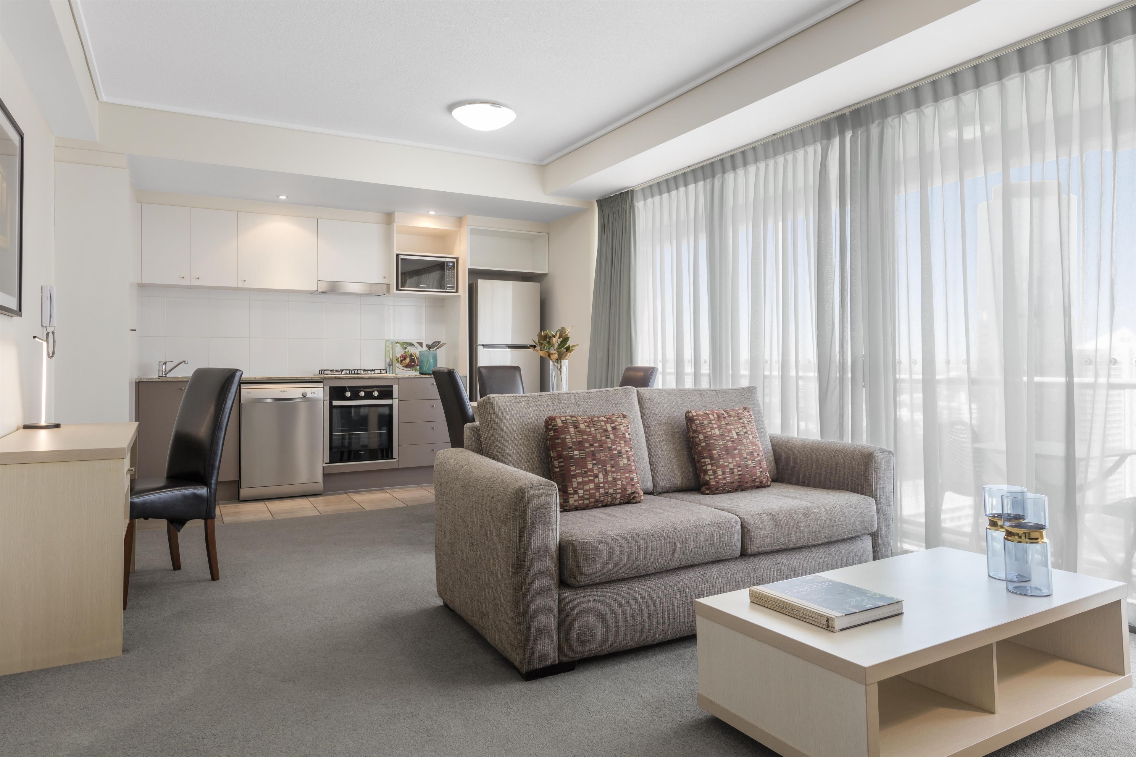 Une chambre d’hôtel moderne équipée d’un canapé, d’une table basse, d’un coin repas avec un four à micro-ondes et d’une cuisine.