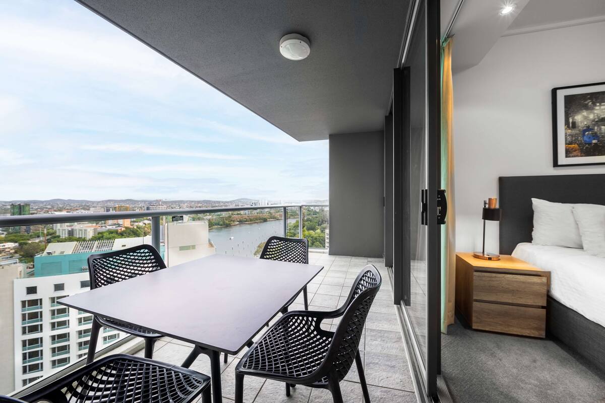 Ein Balkon mit Tisch und Stühlen, ein Bett mit Nachttisch und Blick auf die Stadt.