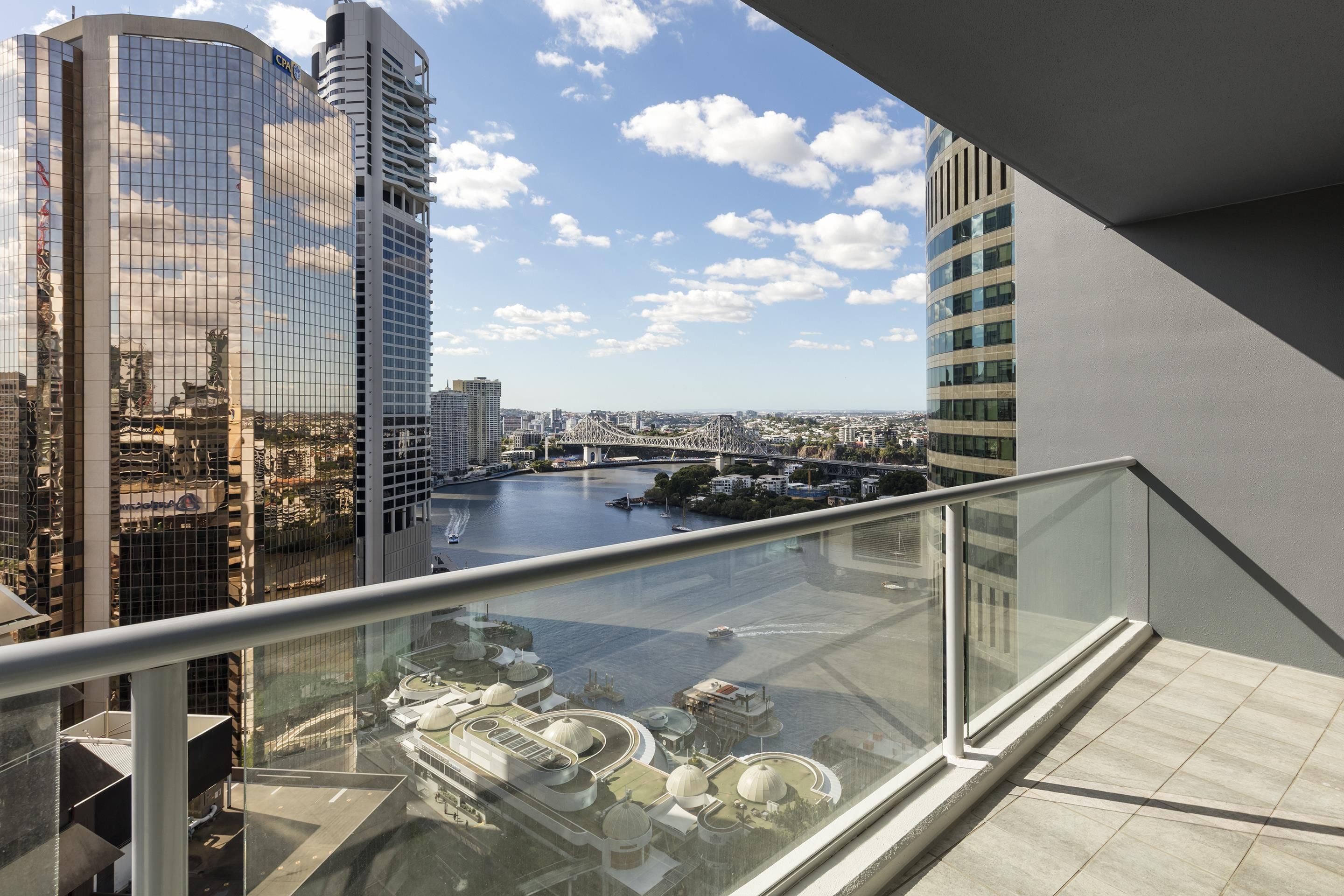A high-rise building with a glass balcony overlooking a river and cityscape.