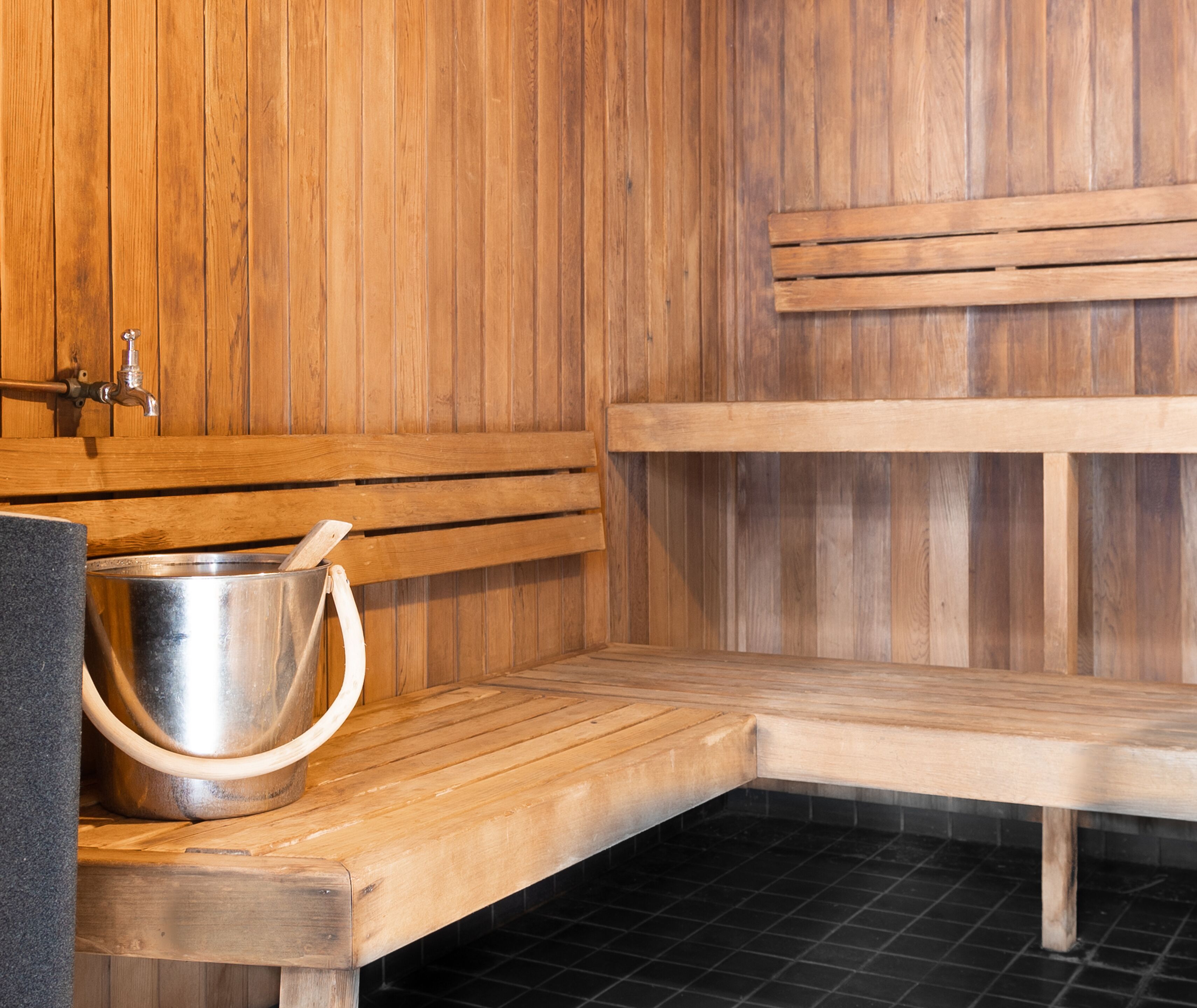 Een sauna met houten banken, een metalen emmer en een kraan.