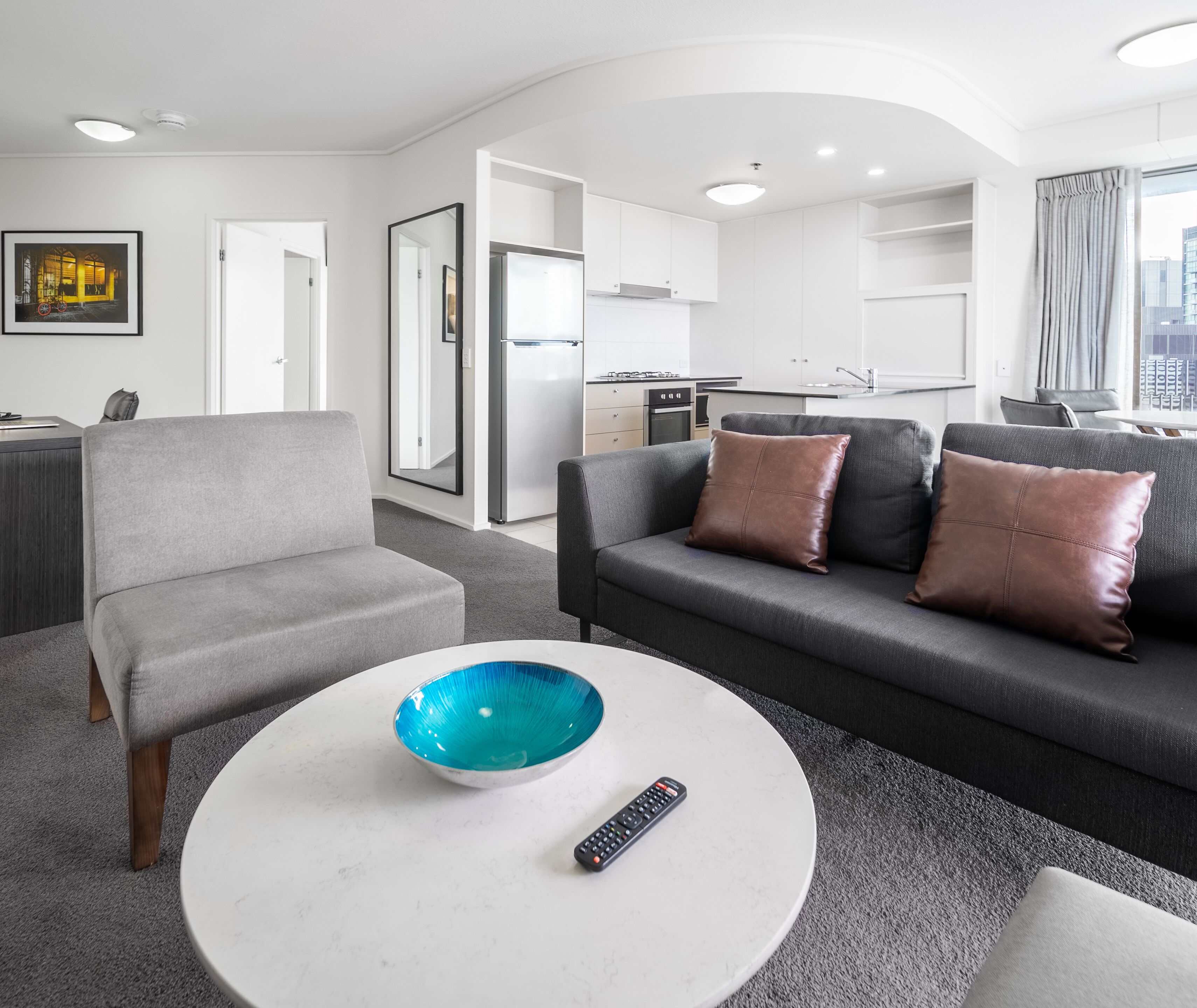 A modern living room with a grey sofa, a round coffee table, and a remote control.