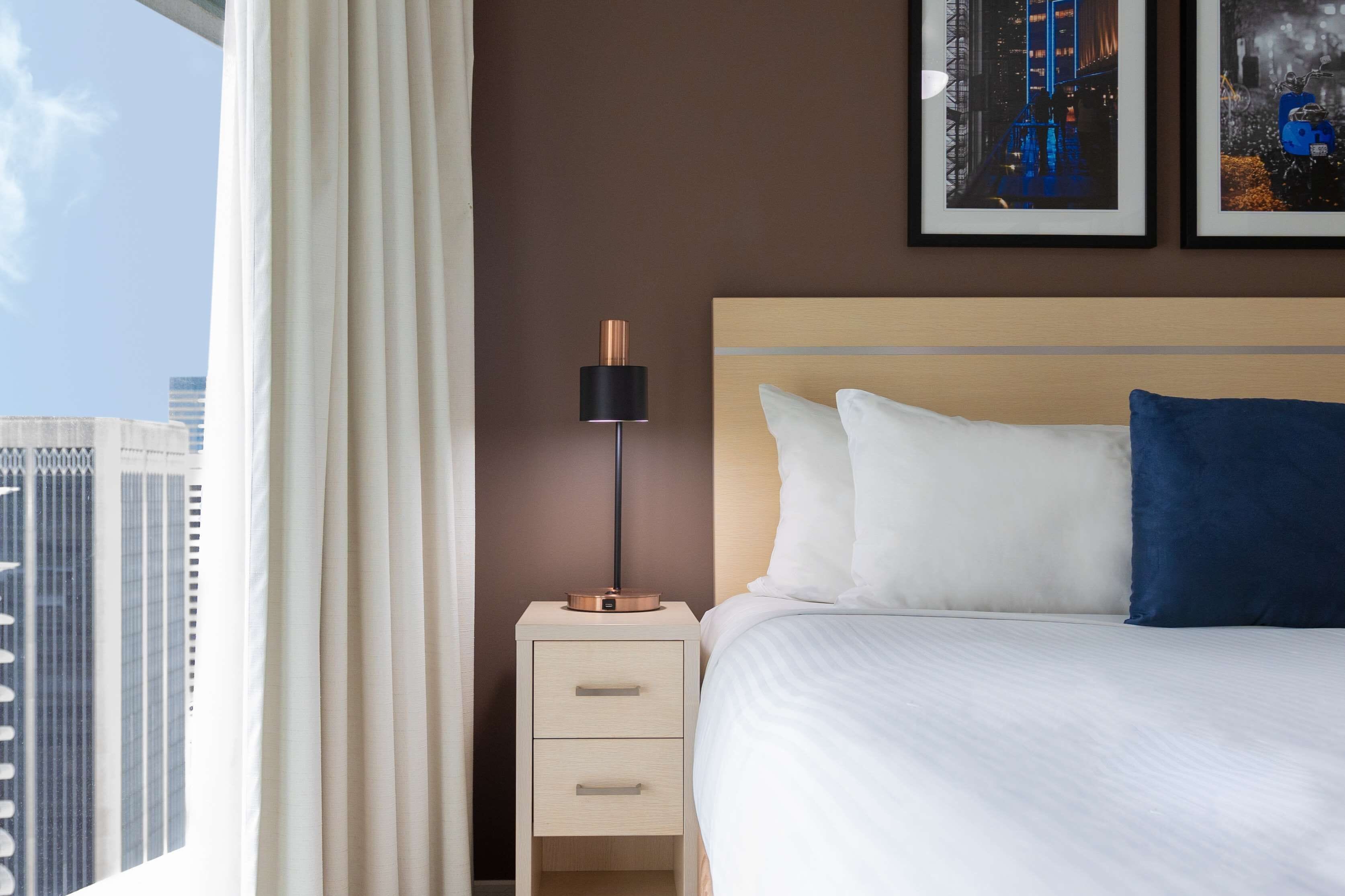 Een hotelkamer met een bed, een nachtkastje, een lamp en twee foto's in lijsten aan de muur.