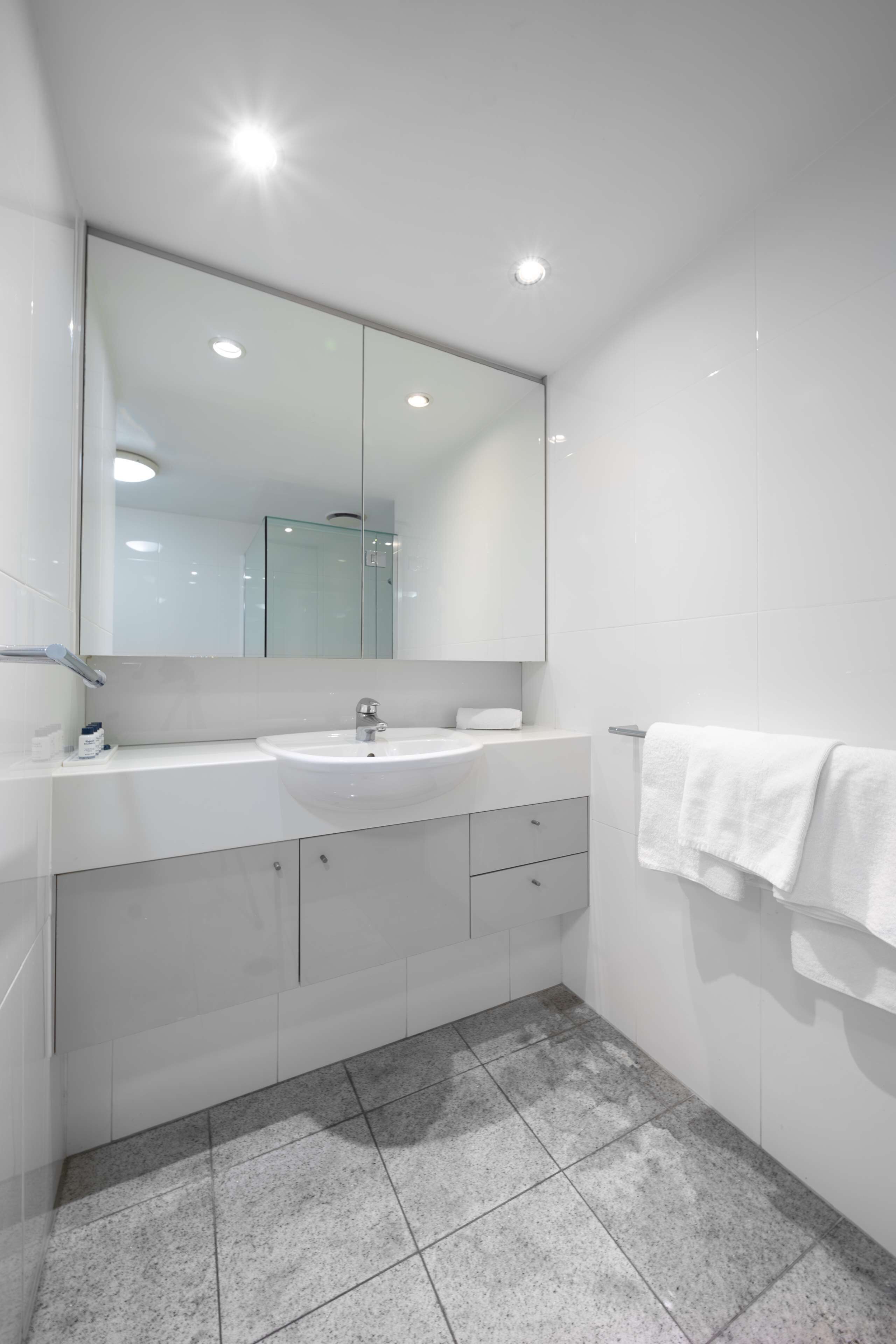 Une salle de bain moderne avec un lavabo blanc, un miroir et un sol carrelé.