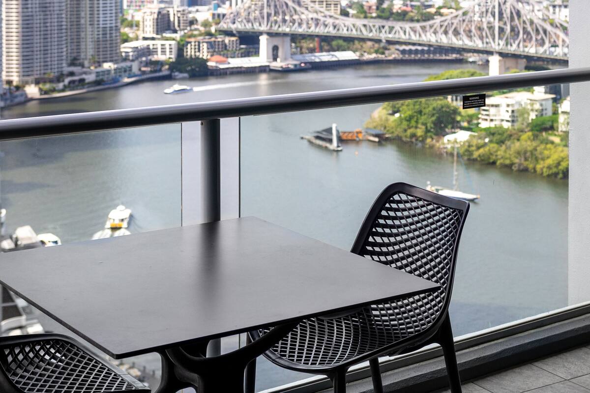 Ein Balkon mit Tisch und Stühlen mit Blick auf eine Stadtlandschaft, inklusive Brücke und Fluss.