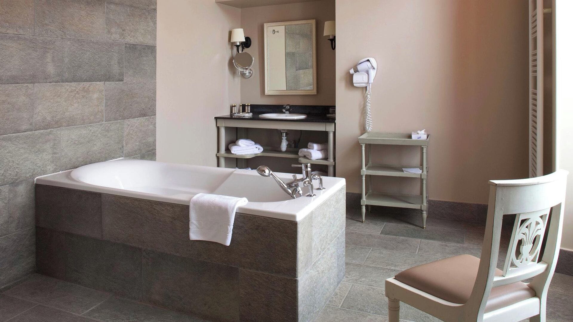 A bathroom with a bathtub, a sink, a mirror, a towel rack, and a chair.