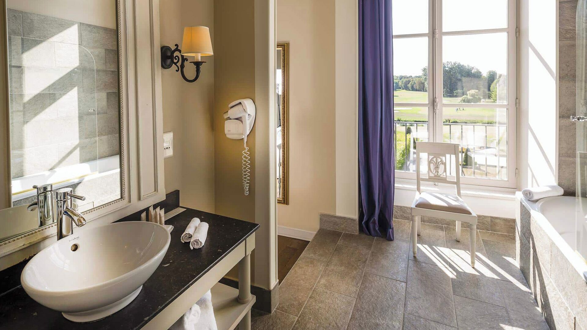 Une salle de bain avec un grand lavabo, un miroir, un porte-serviettes, un téléphone et une vue sur un court de tennis.