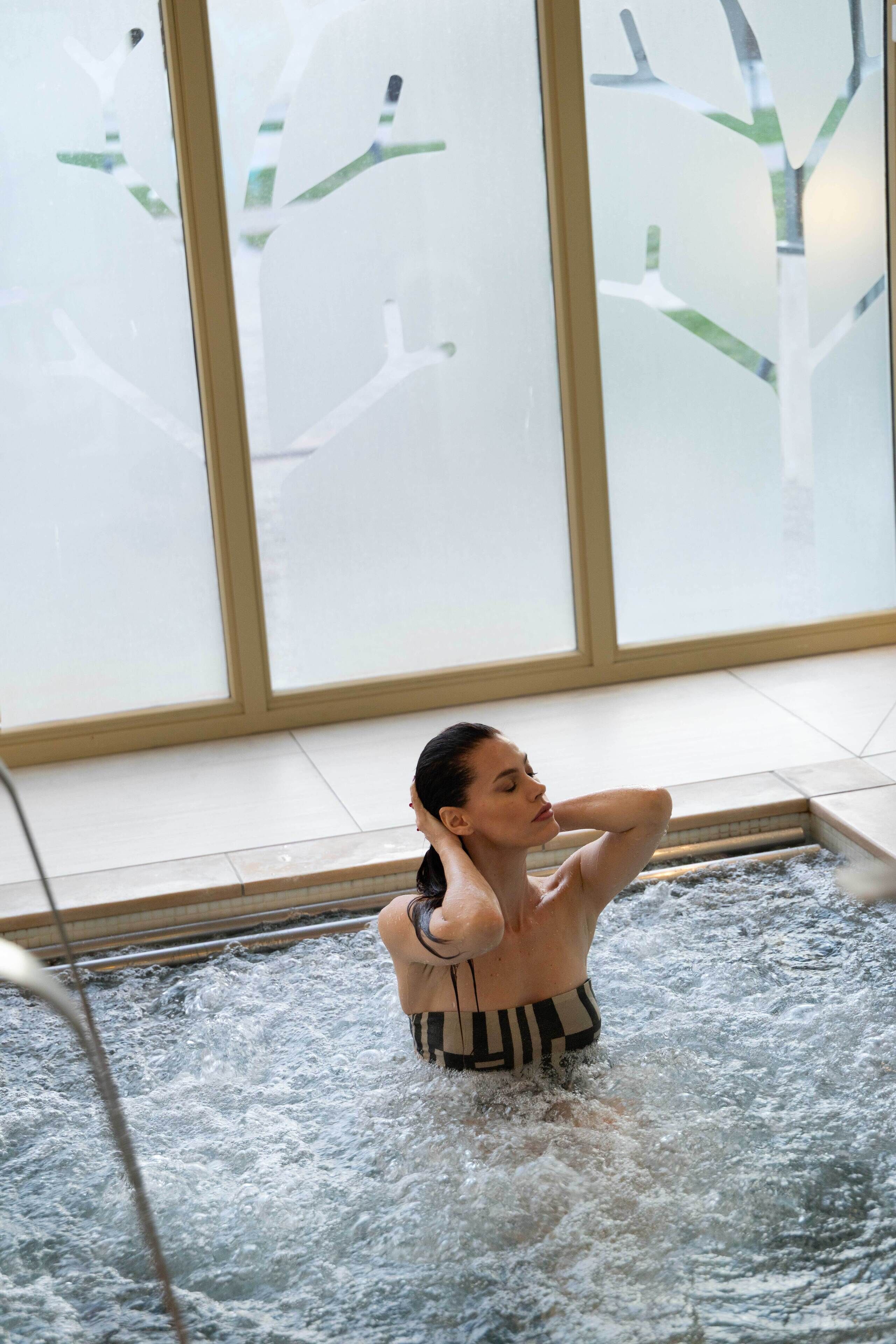 Una persona en un jacuzzi con vistas a ventanales helados y un suelo de baldosas.