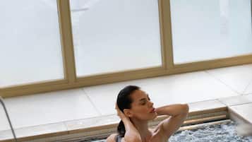 Una persona en un jacuzzi con vistas a ventanales helados y un suelo de baldosas.