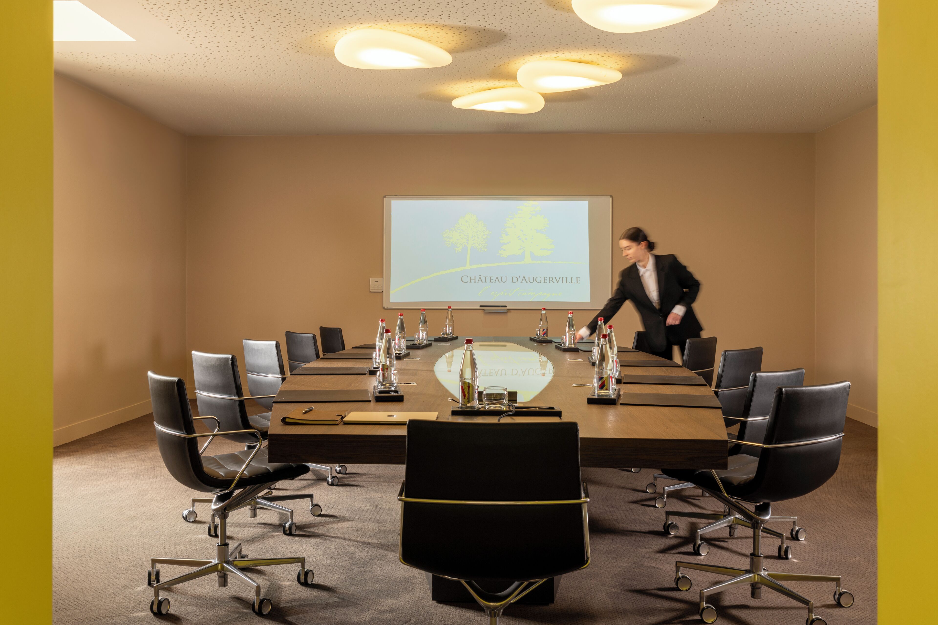 Ett konferensrum med ett stort bord, stolar och en presentationsskärm som visar texten ”CHÂTEAU D’AUGERVILLE”.