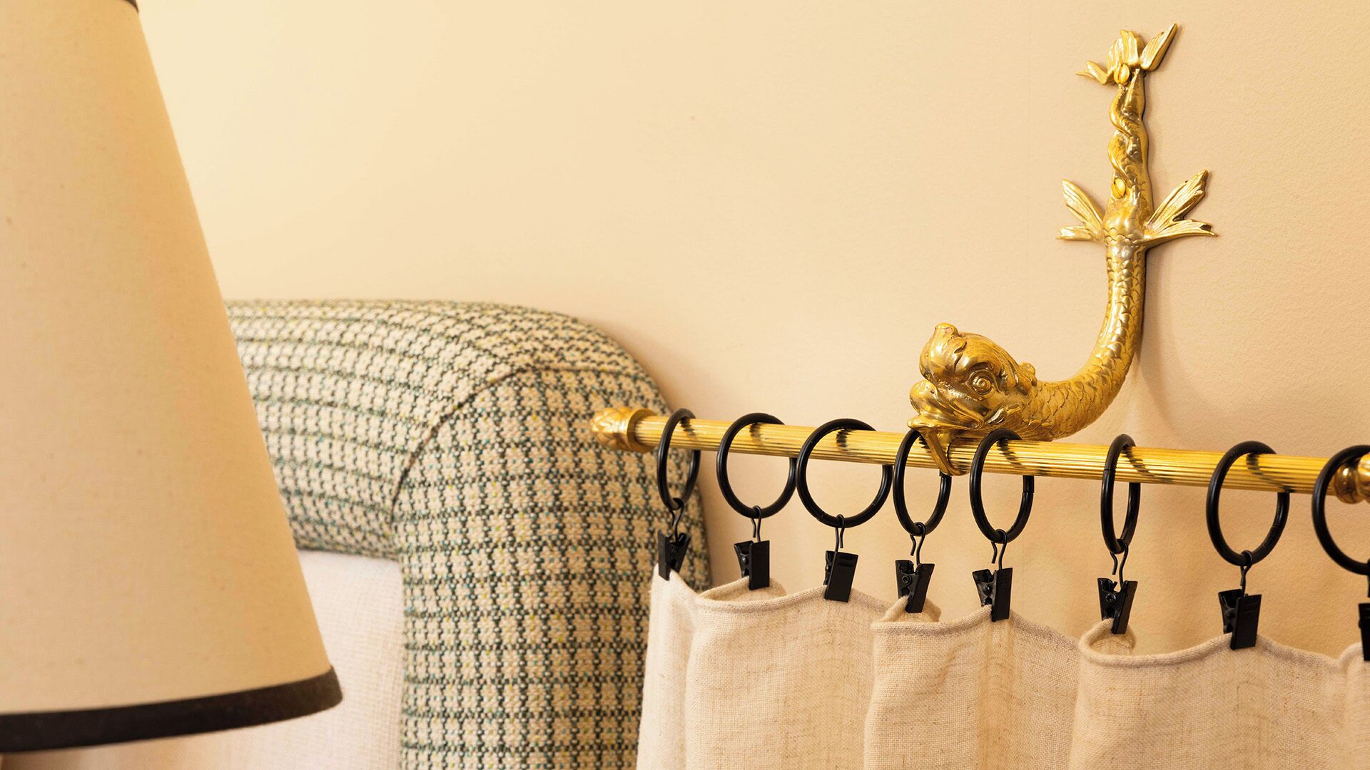 A curtain rod with a golden fish decoration, a lamp, and a patterned cushion.